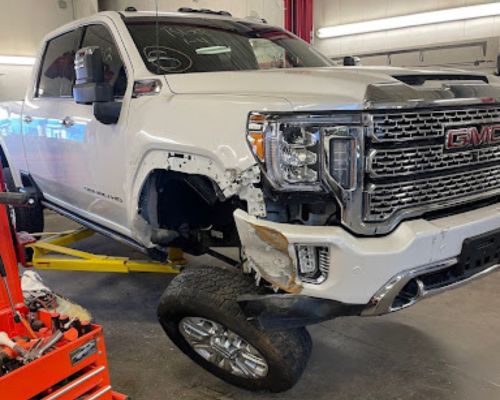 Trusted Collision Center in Iowa City | Harv’s Auto Body Repair. Image of white pickup truck with front end damage due to a collision in shop for repairs.