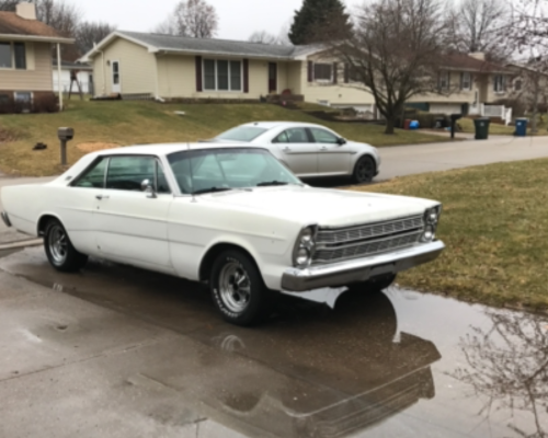 This image is a before image of a white Classic Ford Galaxie needing a new custom paint job with Harv’s Auto Body and Repair in Iowa City, IA parked in owners driveway.