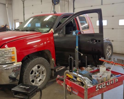Collision Repair and Auto Body Repair in Iowa City, IA at Harv’s Auto Body. Image of a red truck with an open door undergoing repair for car door dings and dents after a collision