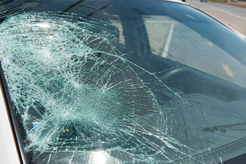 Looking for auto glass replacement services in Iowa City, IA. Call Harv’s Auto Body. Image of damaged car windshield on passenger side of silver car from vehicle accident.