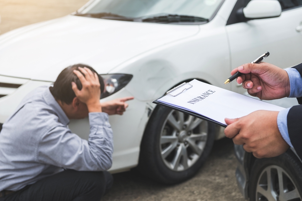 Auto Insurance Claim in Iowa City, IA by Harv’s Auto Body Repair. Image of a man assessing collision damage after a summer accident.